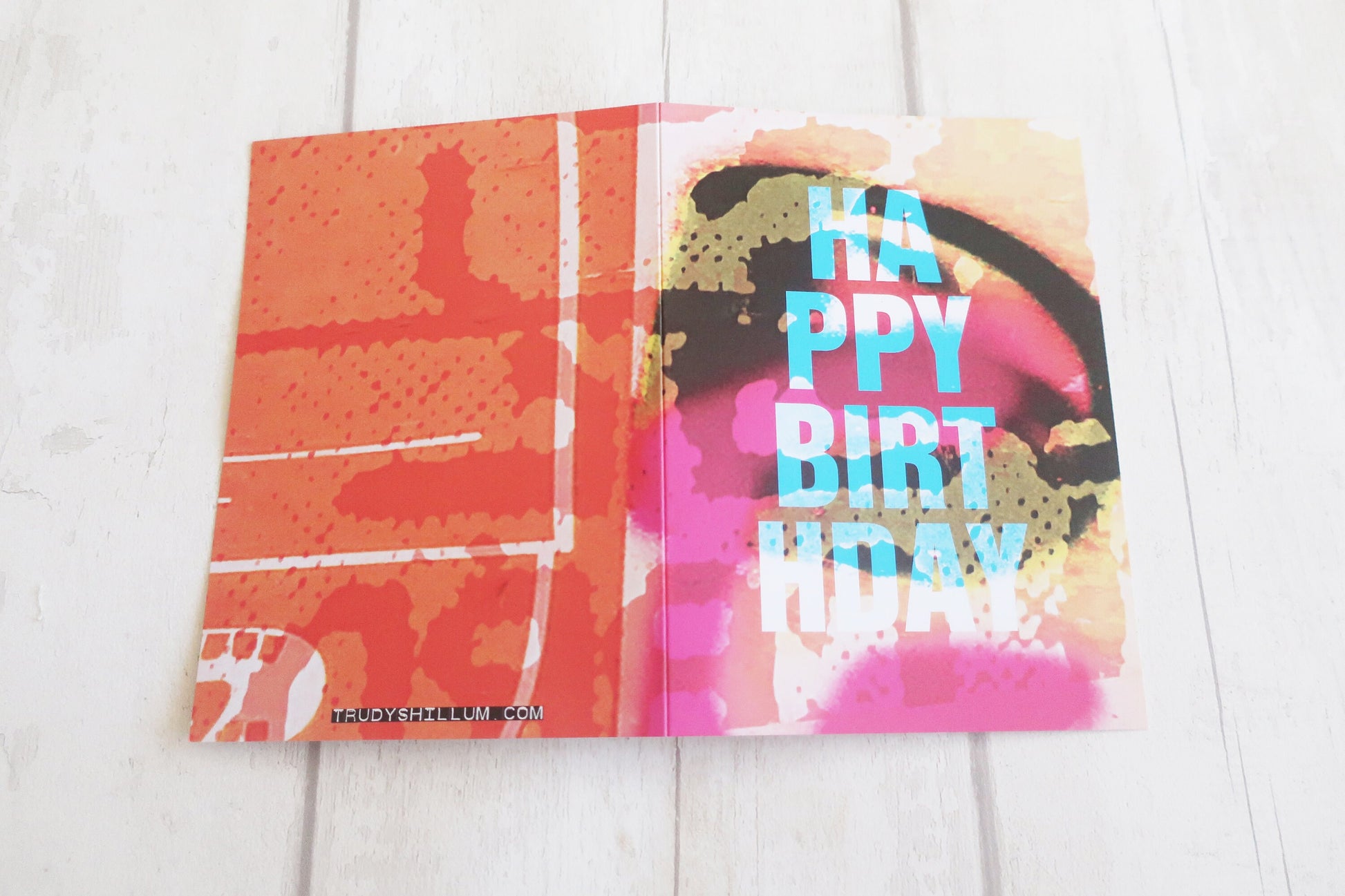 Colorful birthday card with abstract designs and 'Happy Birthday' text on a white wooden surface.