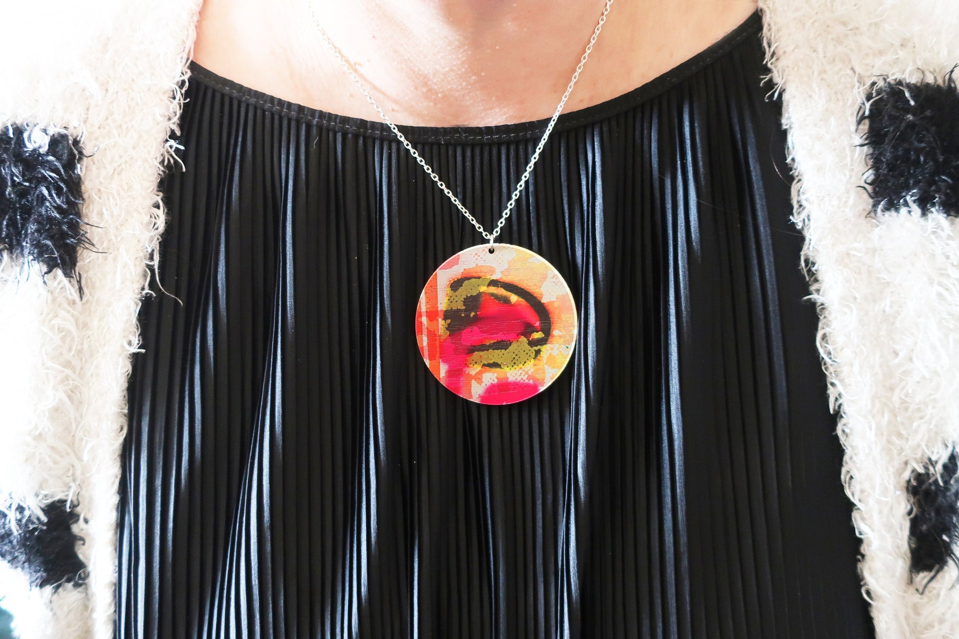 Person wearing a black pleated dress with a colorful pendant necklace.