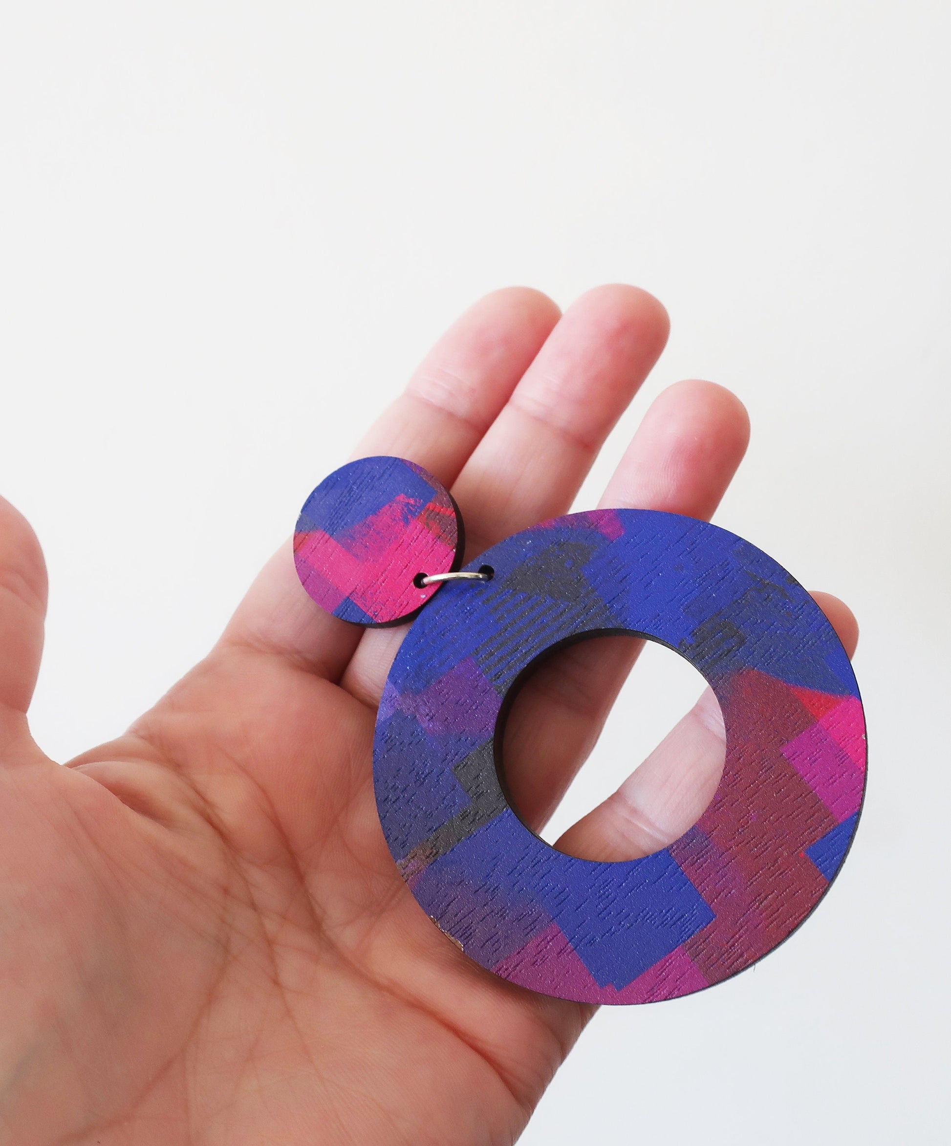 Hand holding colorful circular earring against a white background