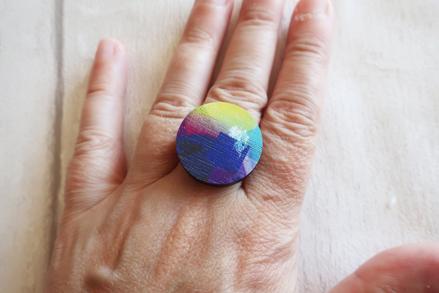 Hand wearing a colorful ring on a light background