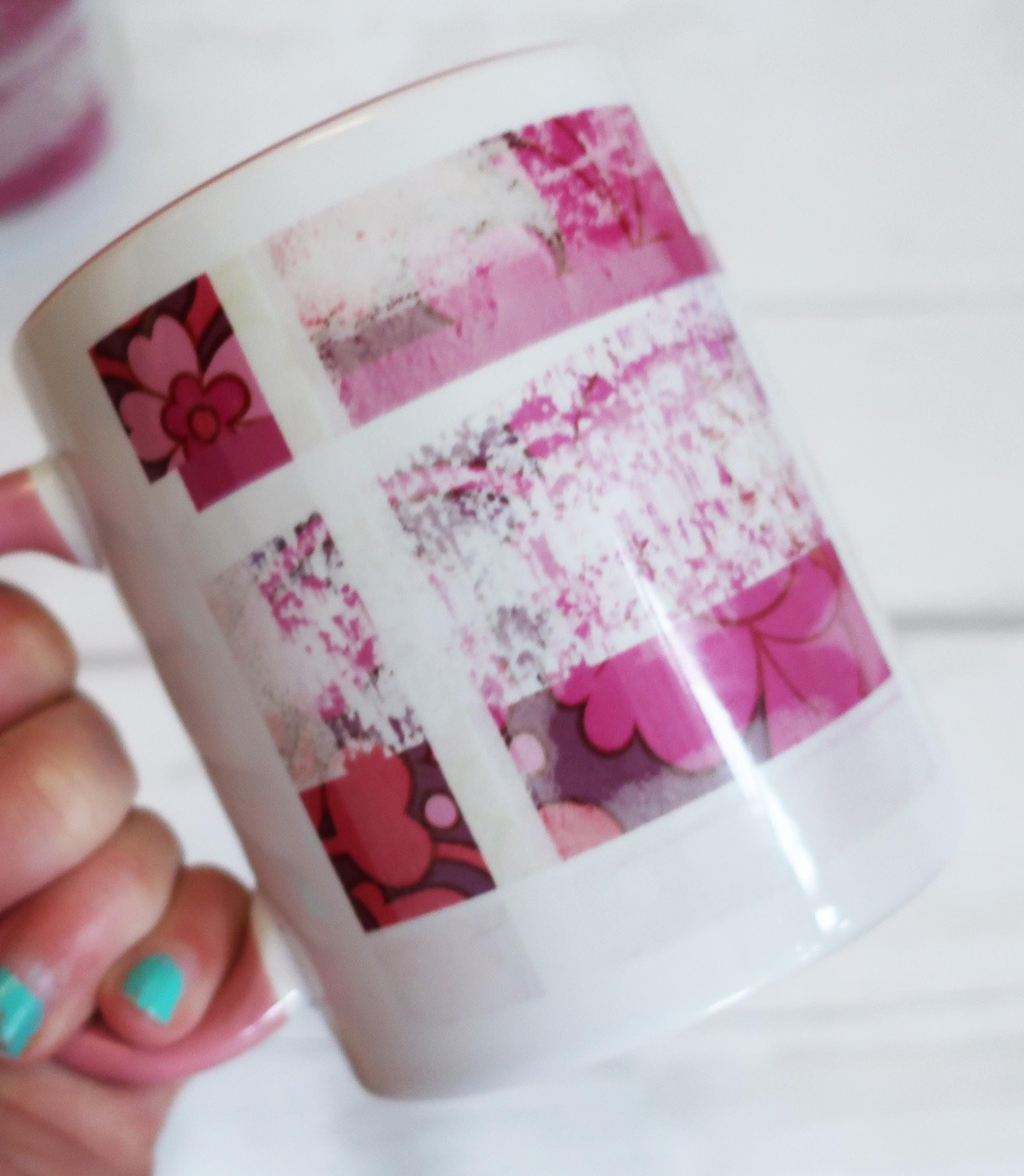 White mug with pink floral patterns held by a hand with turquoise nail polish.