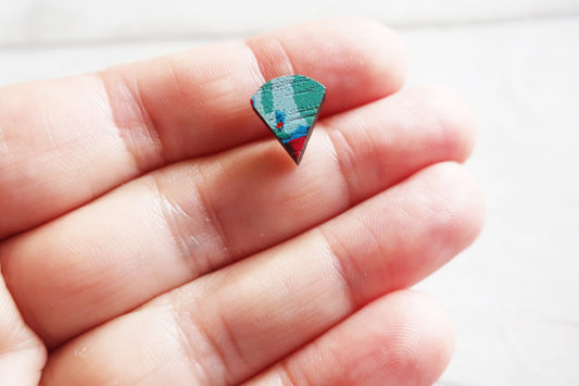 Small colorful triangular earring  held between fingers against a light background