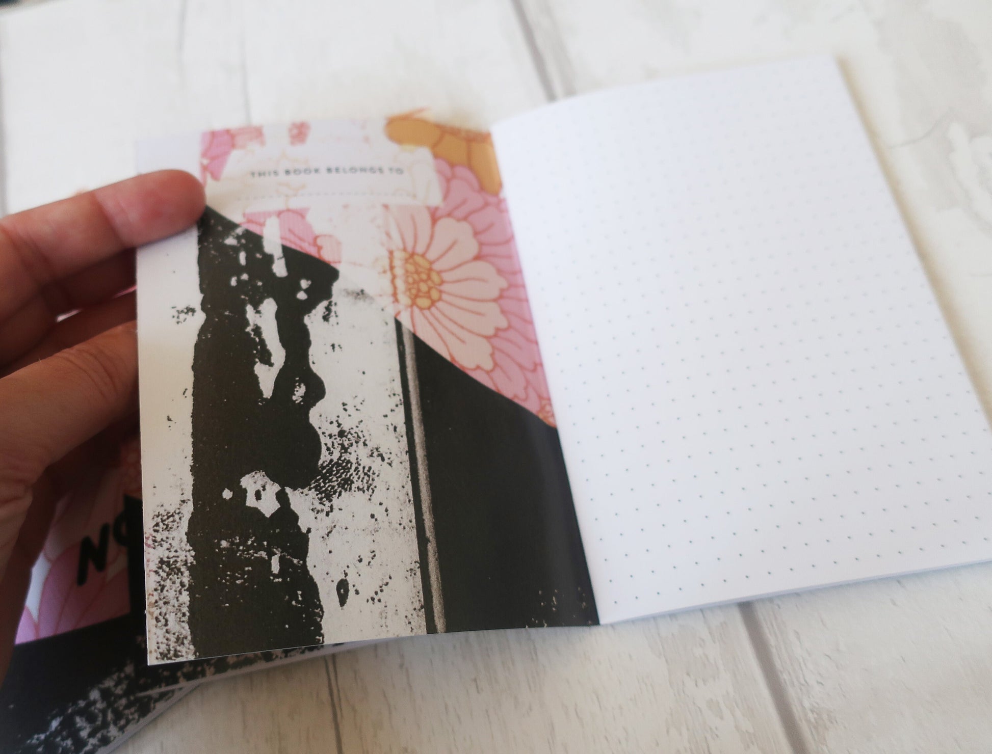 Hand holding a notebook with floral and black abstract design on a white surface