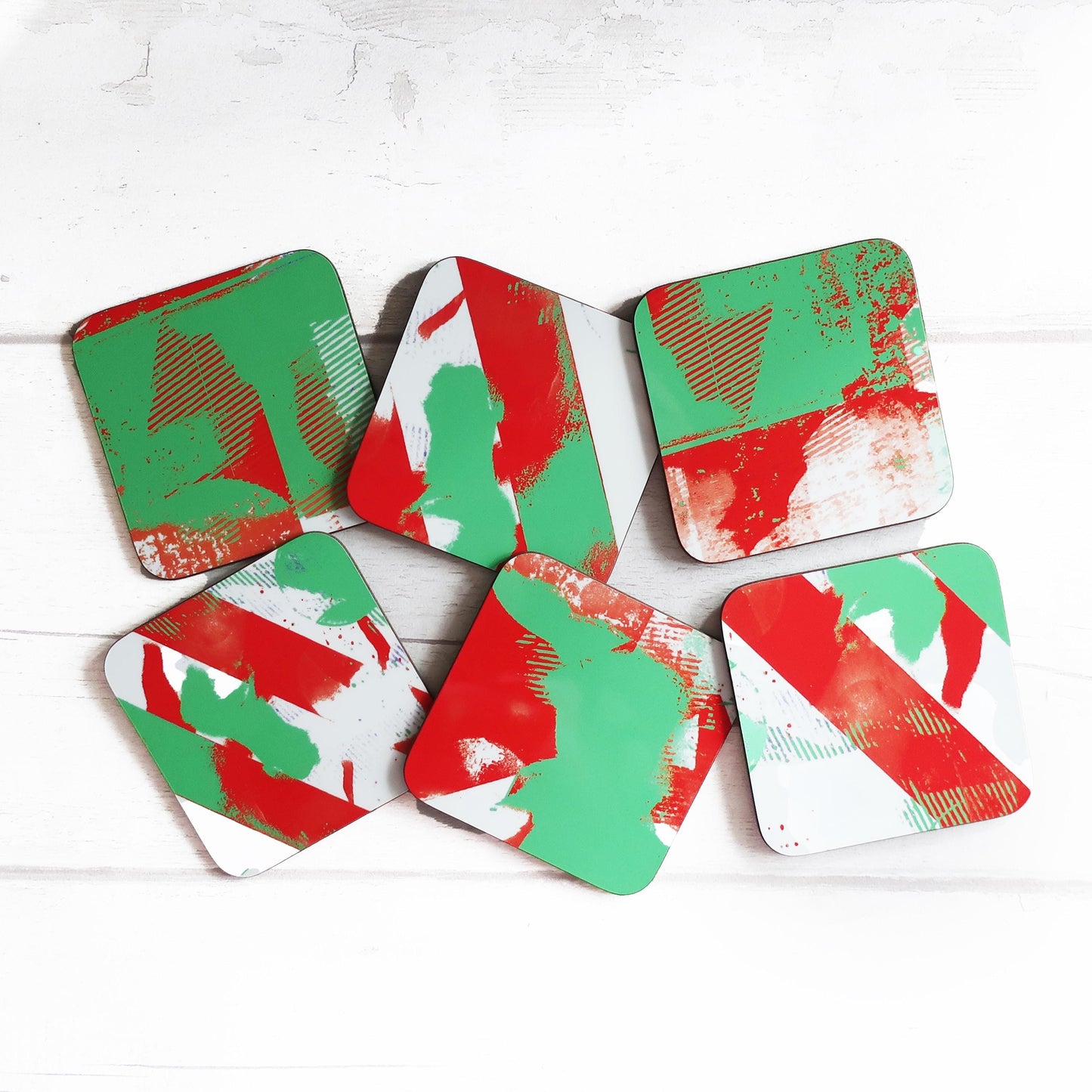 Set of six geometric coasters with red and green patterns on a white wooden surface