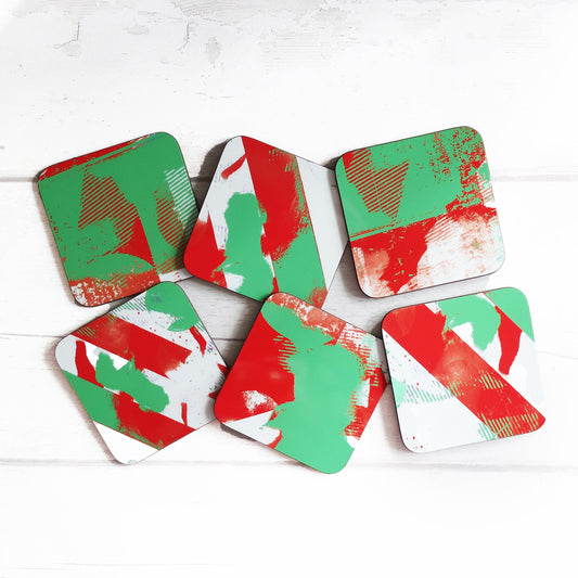Set of six geometric coasters with red and green patterns on a white wooden surface