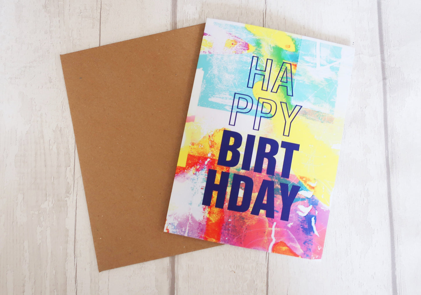 Colorful 'Happy Birthday' card with a brown envelope on a light wooden surface