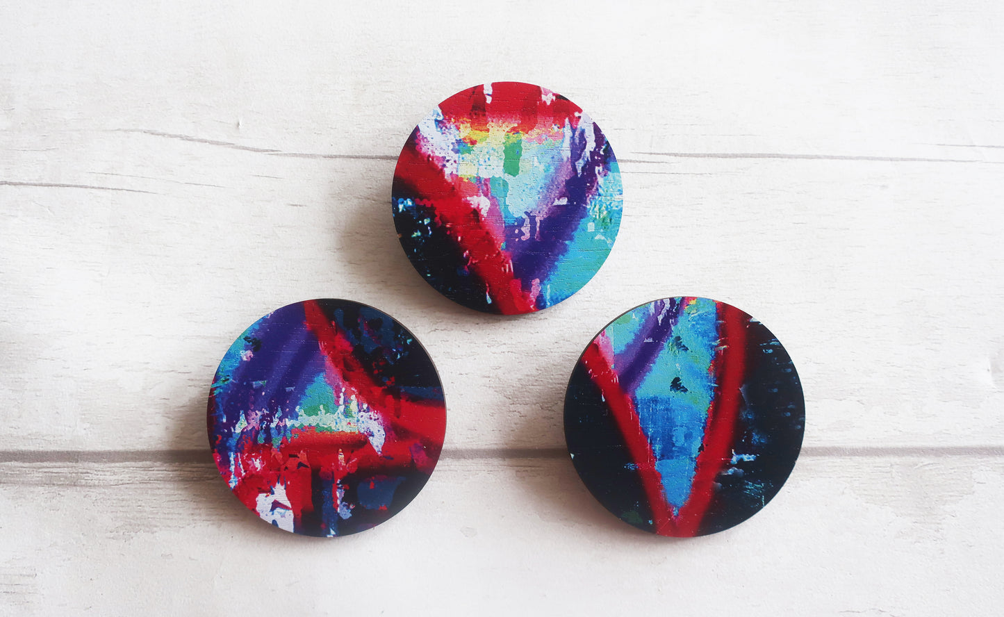 Three colorful circular brooches with abstract patterns on a white wooden surface