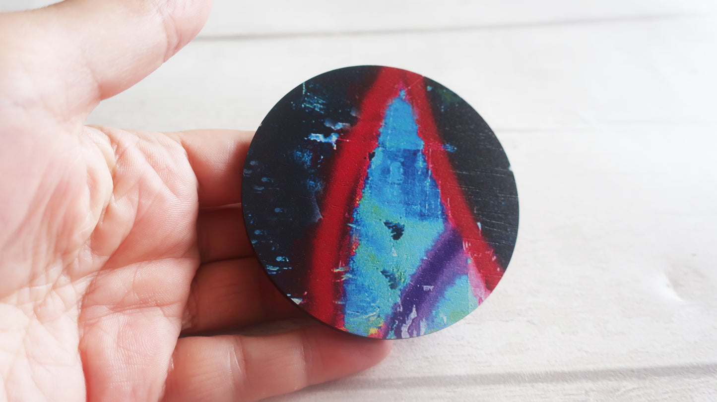 Hand holding a round, colorful brooch with abstract design on a light background