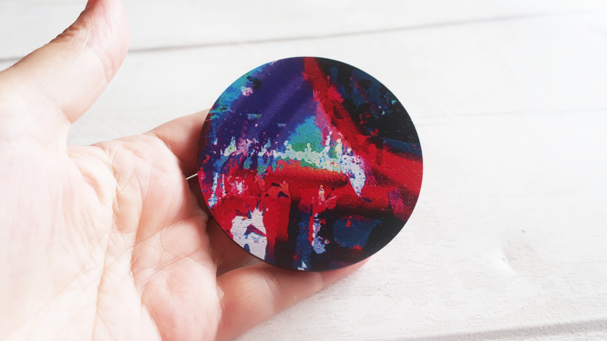 Colorful circular brooch held by a hand on a white background