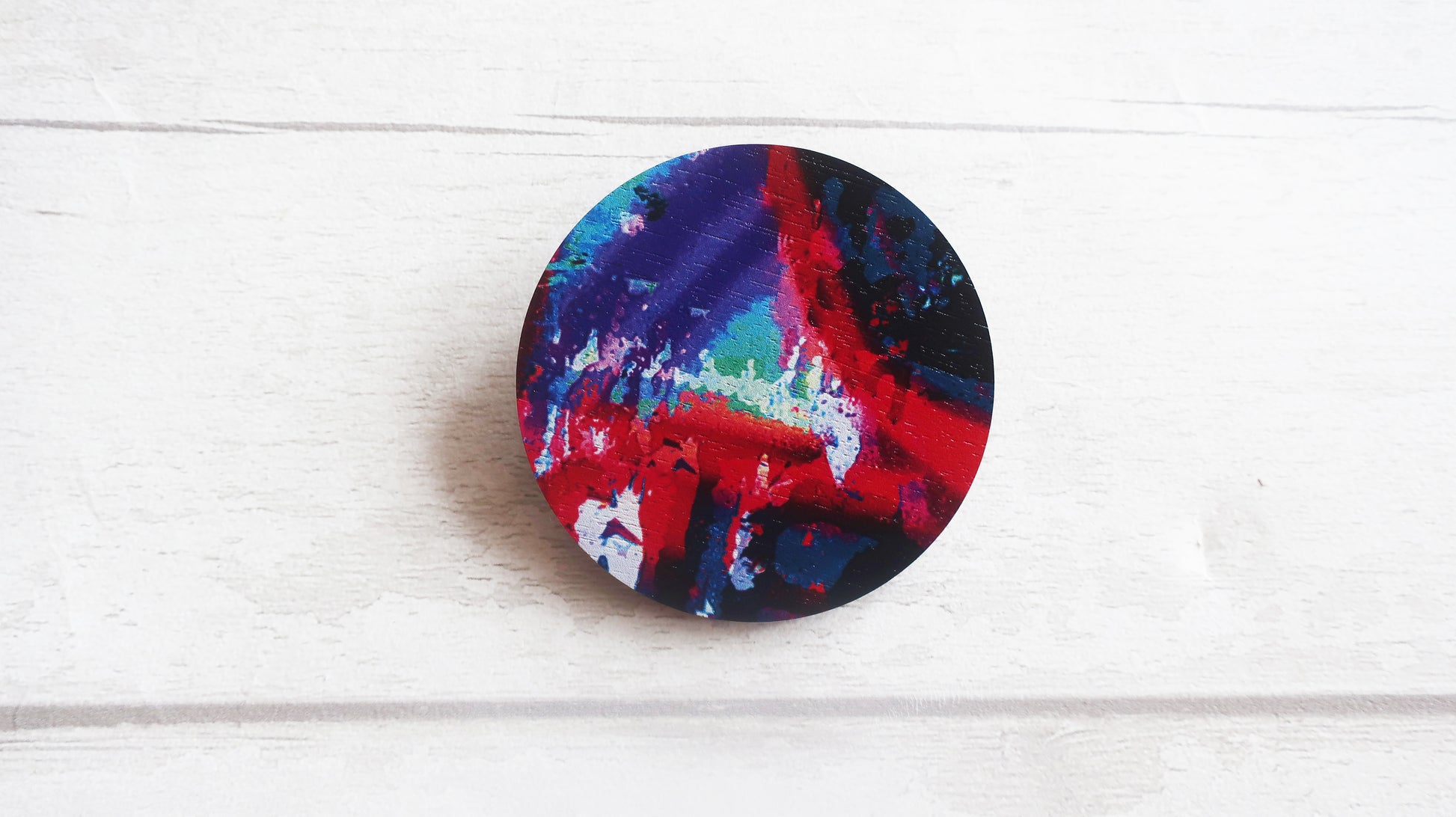 Colorful abstract design on a round brooch against a white background