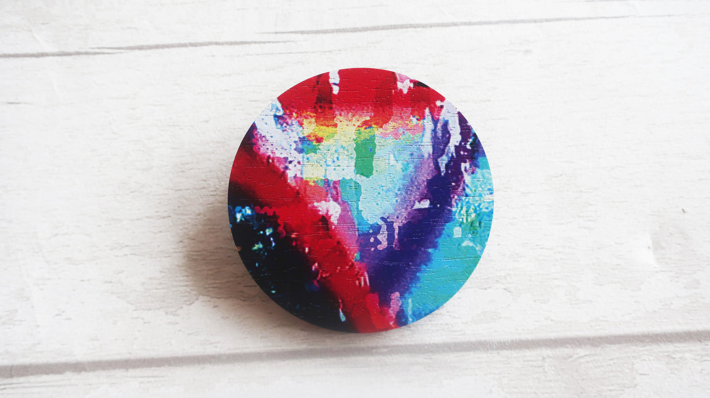 Colorful circular brooch with a rainbow pattern on a light wooden surface