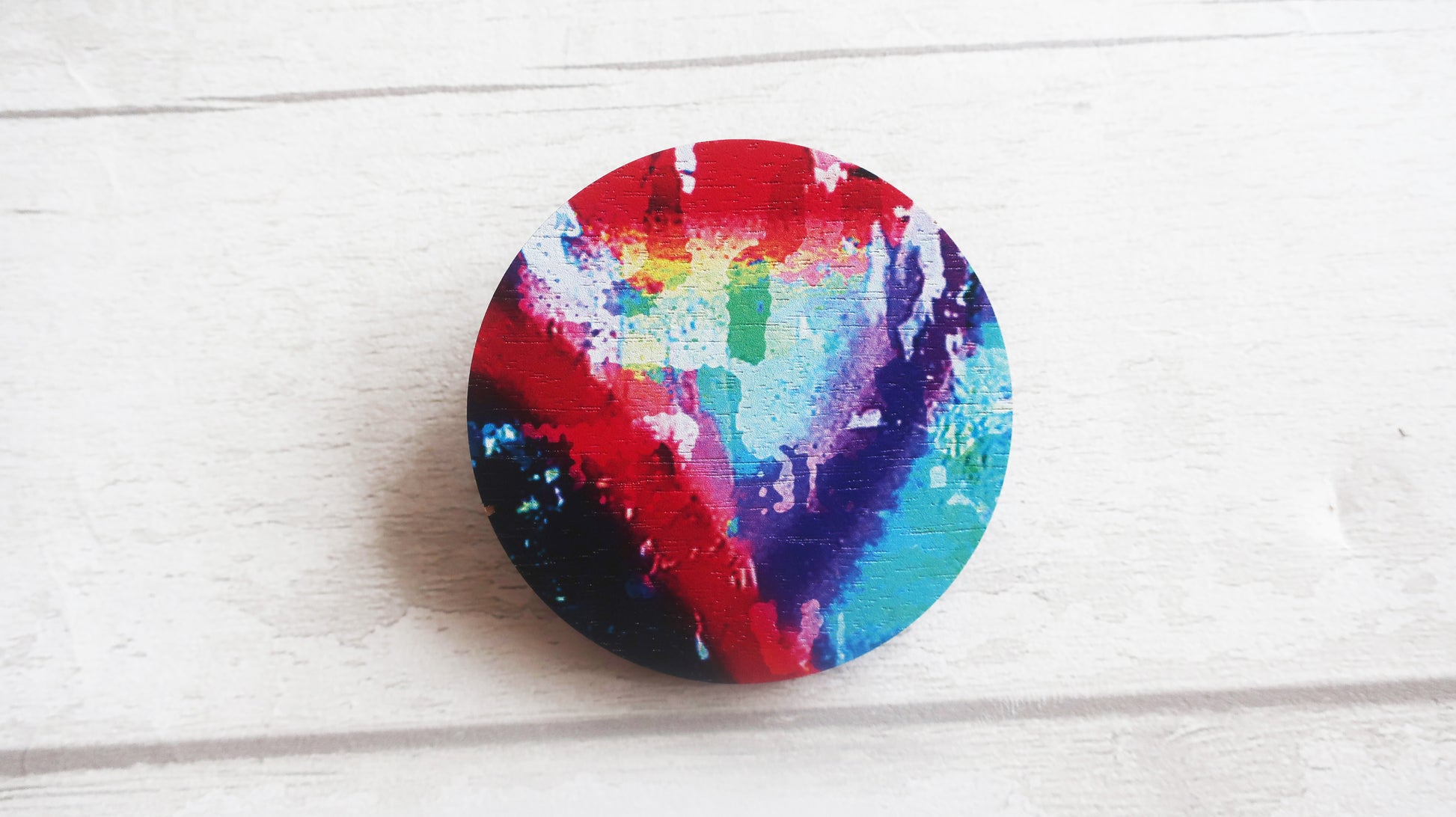 Colorful circular brooch with a rainbow pattern on a light wooden surface