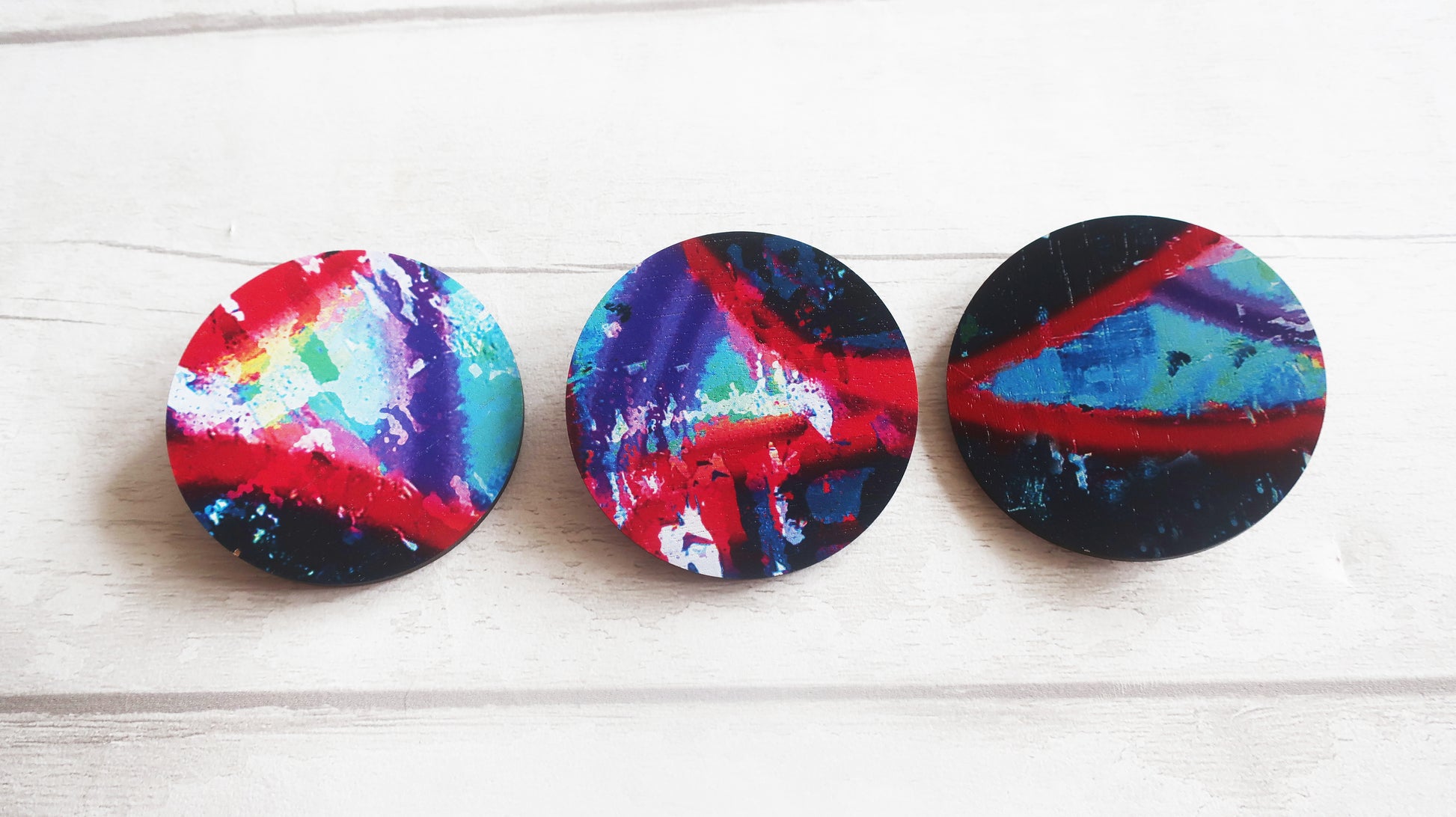 Three colorful circular brooches  with abstract patterns on a white wooden surface