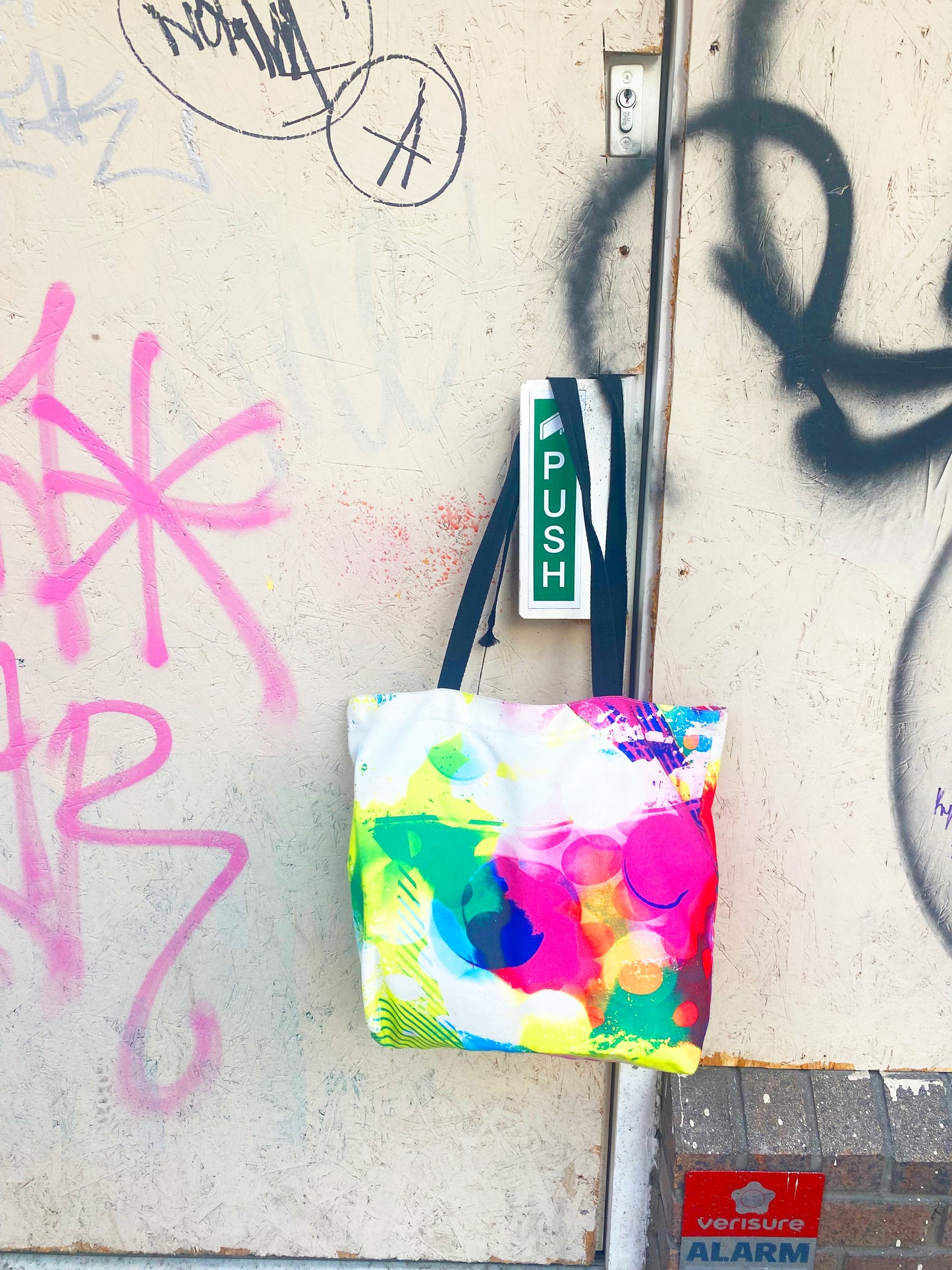Colorful tote bag with abstract design attached to a wall with graffiti