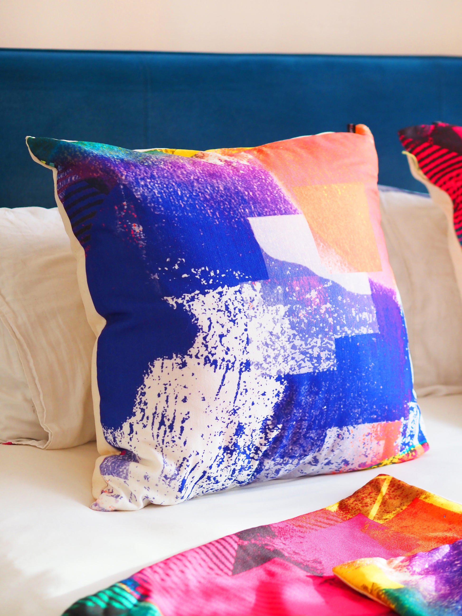 Colorful abstract-patterned pillow on a couch with a blue headboard.