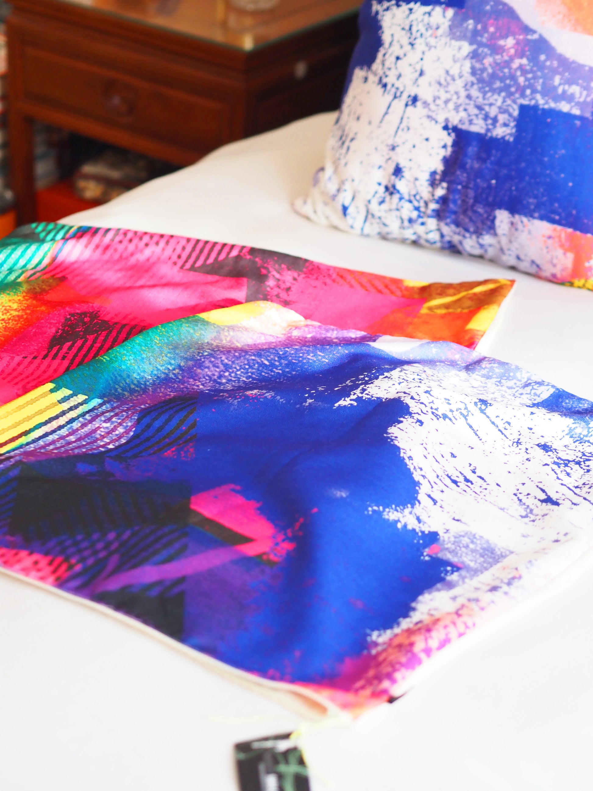 Colorful abstract cushion cover on a bedspread with a pillow in the background.