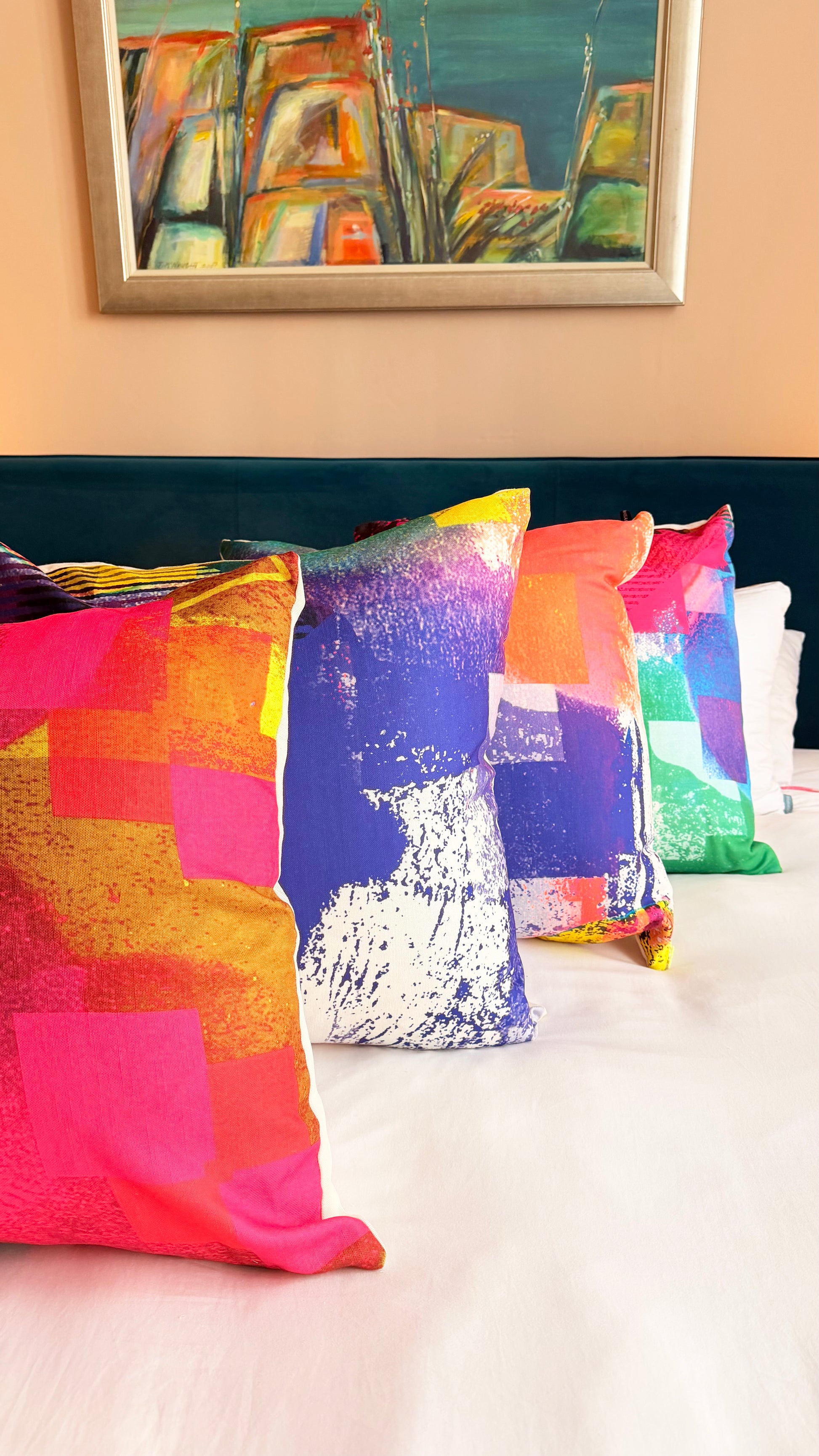 Colorful abstract cushions on a bed with a painting in the background