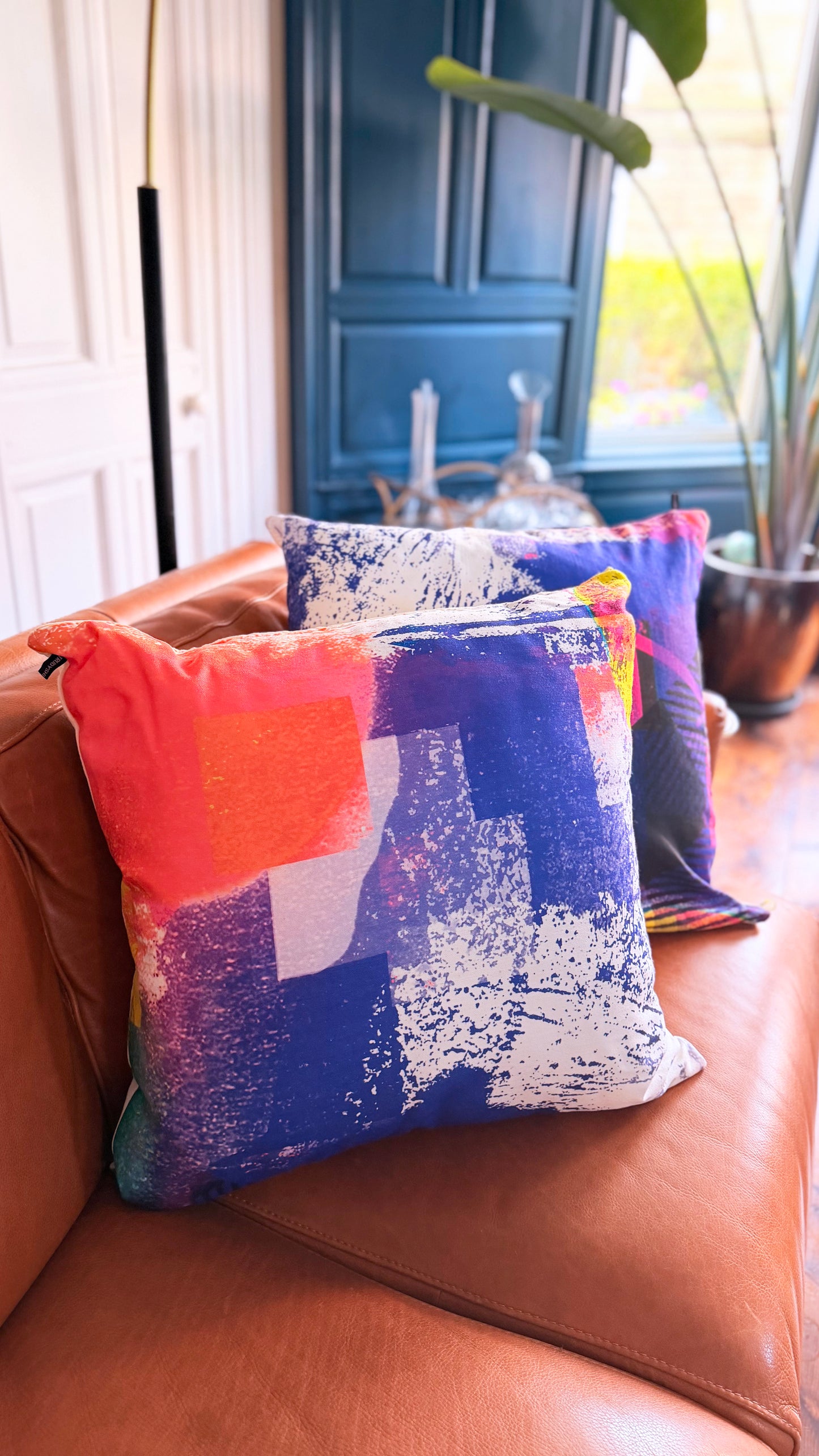 Colorful abstract-patterned pillow on a brown leather couch with a blurred background