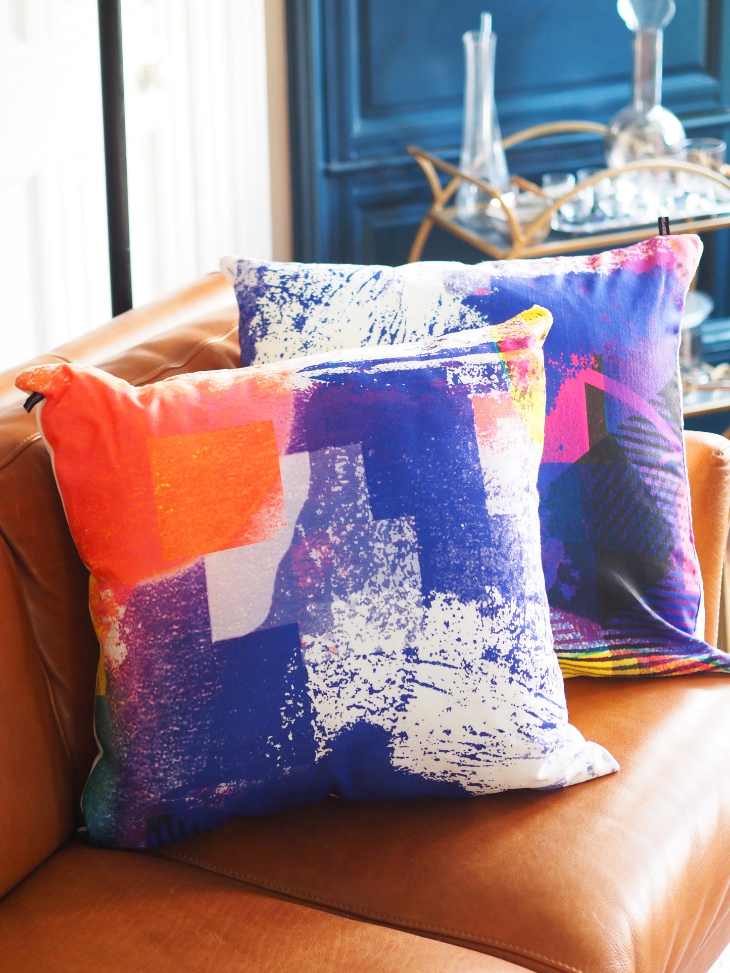 Colorful abstract-patterned pillows on a brown leather couch.