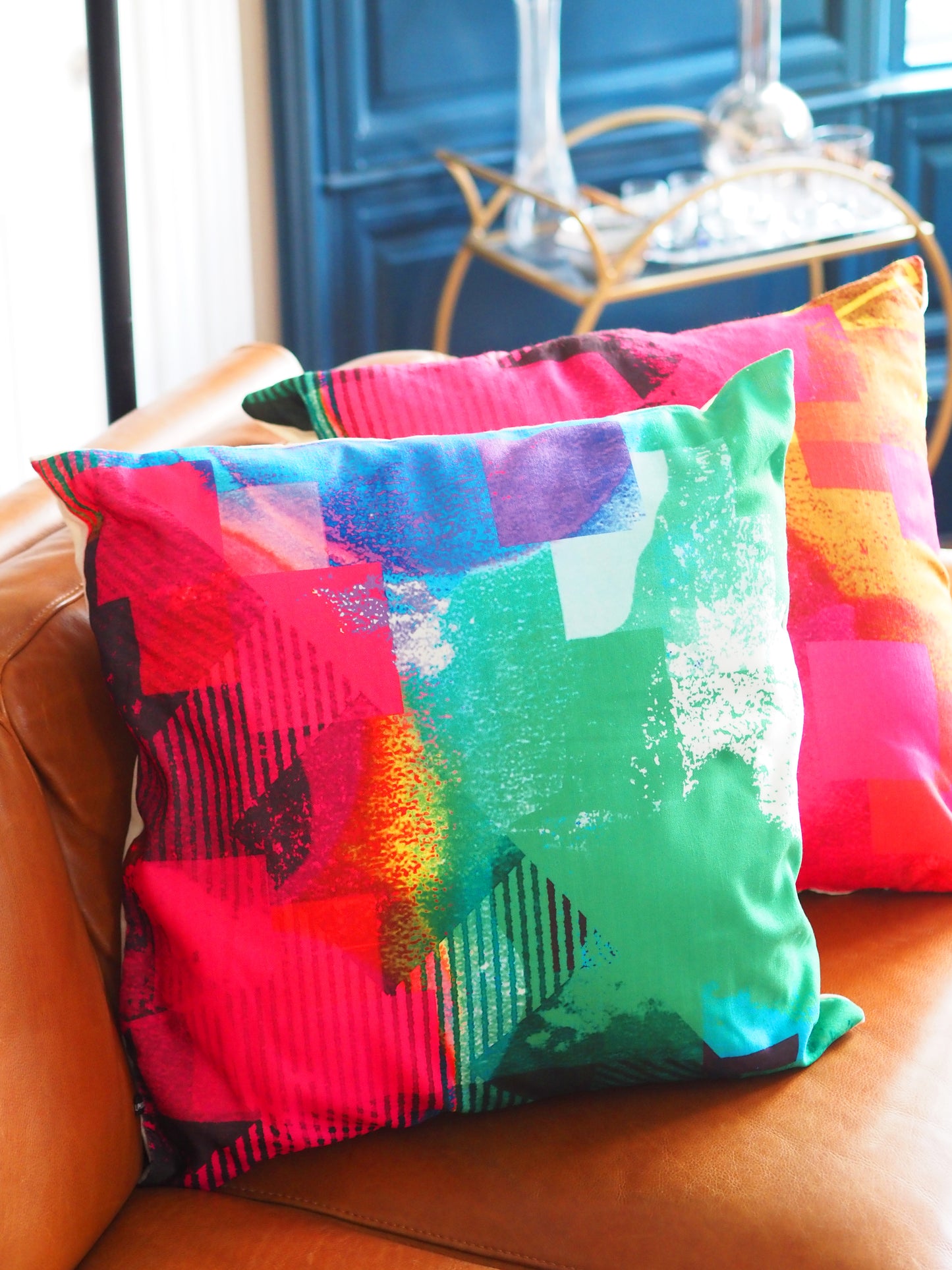 Colorful abstract-patterned pillows on a brown leather couch.