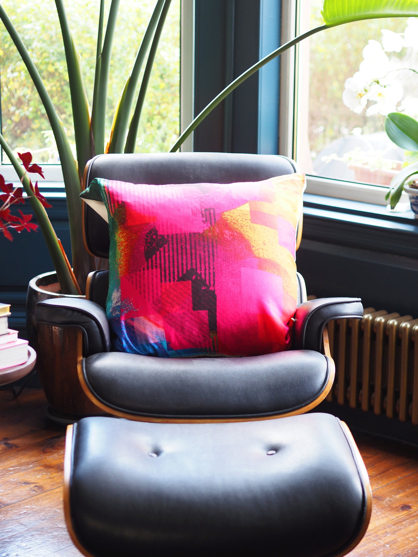 Chair with a colorful pillow in a room with plants and a window.