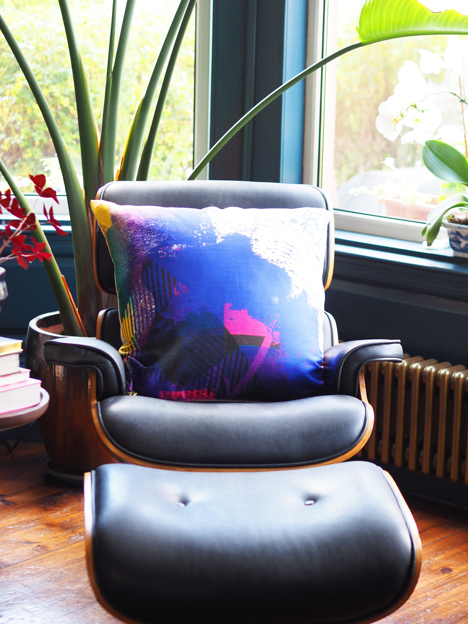 Gray armchair with a colorful pillow in a room with large windows and plants.