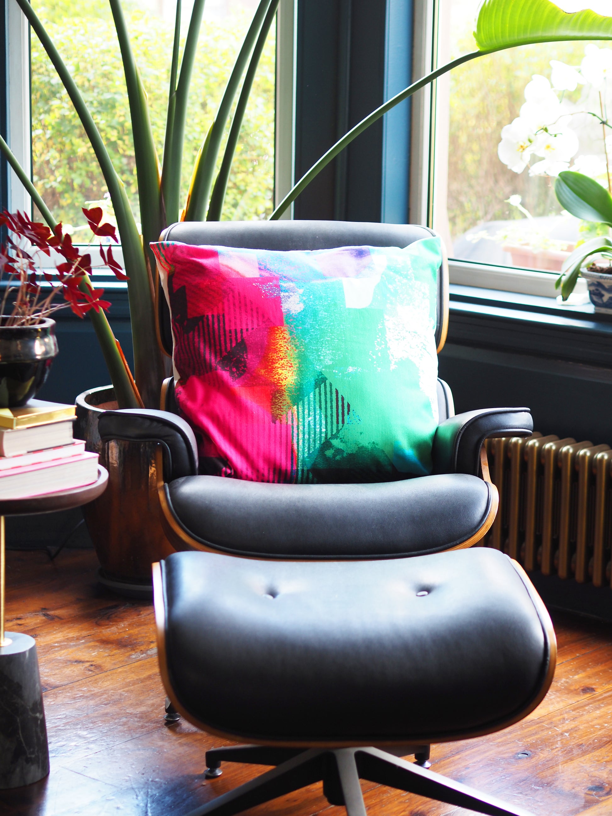 Eames-style chair with a colorful pillow in a room with large windows and plants.