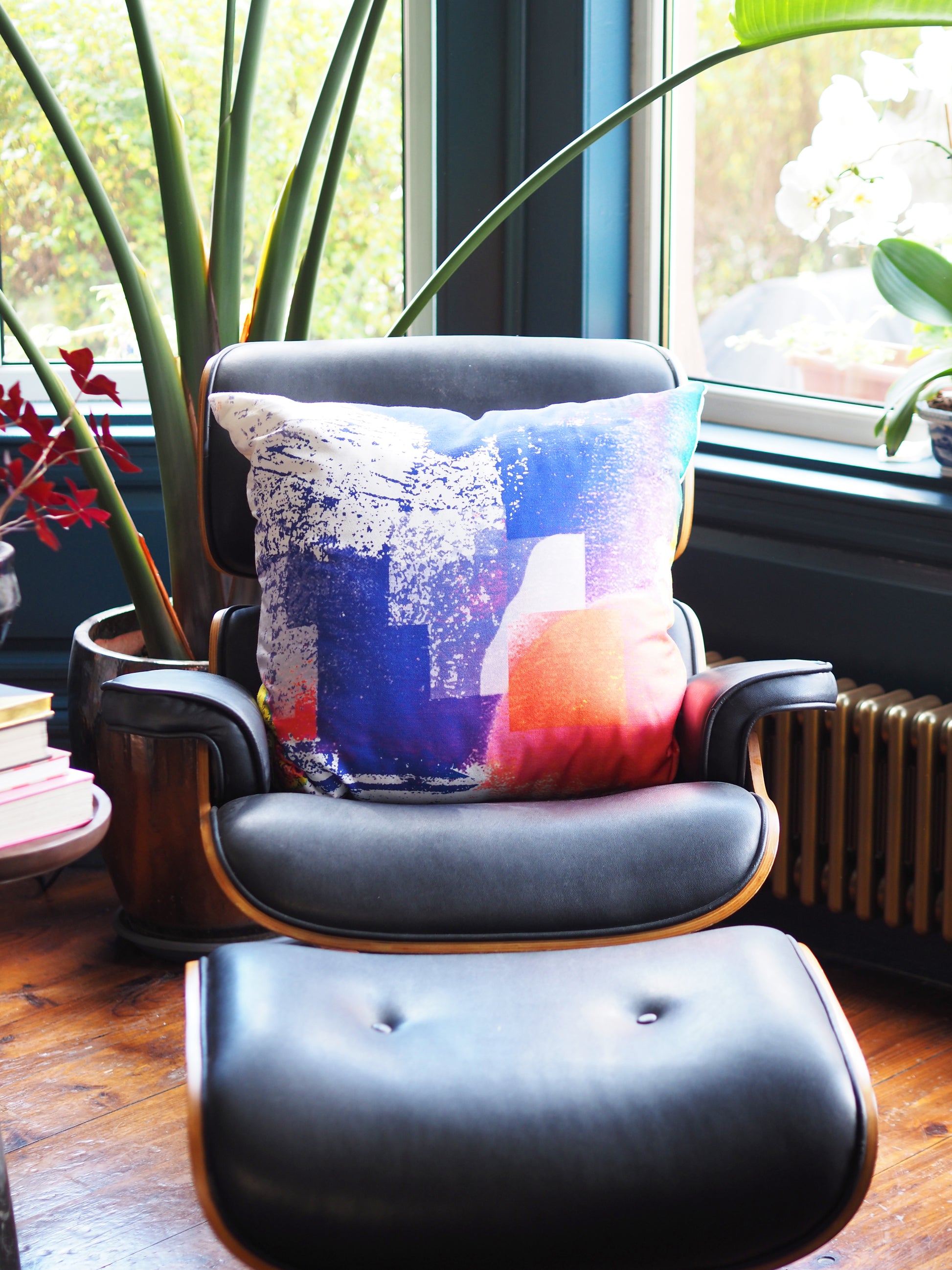 Chair with a colorful pillow in a room with large windows and plants.