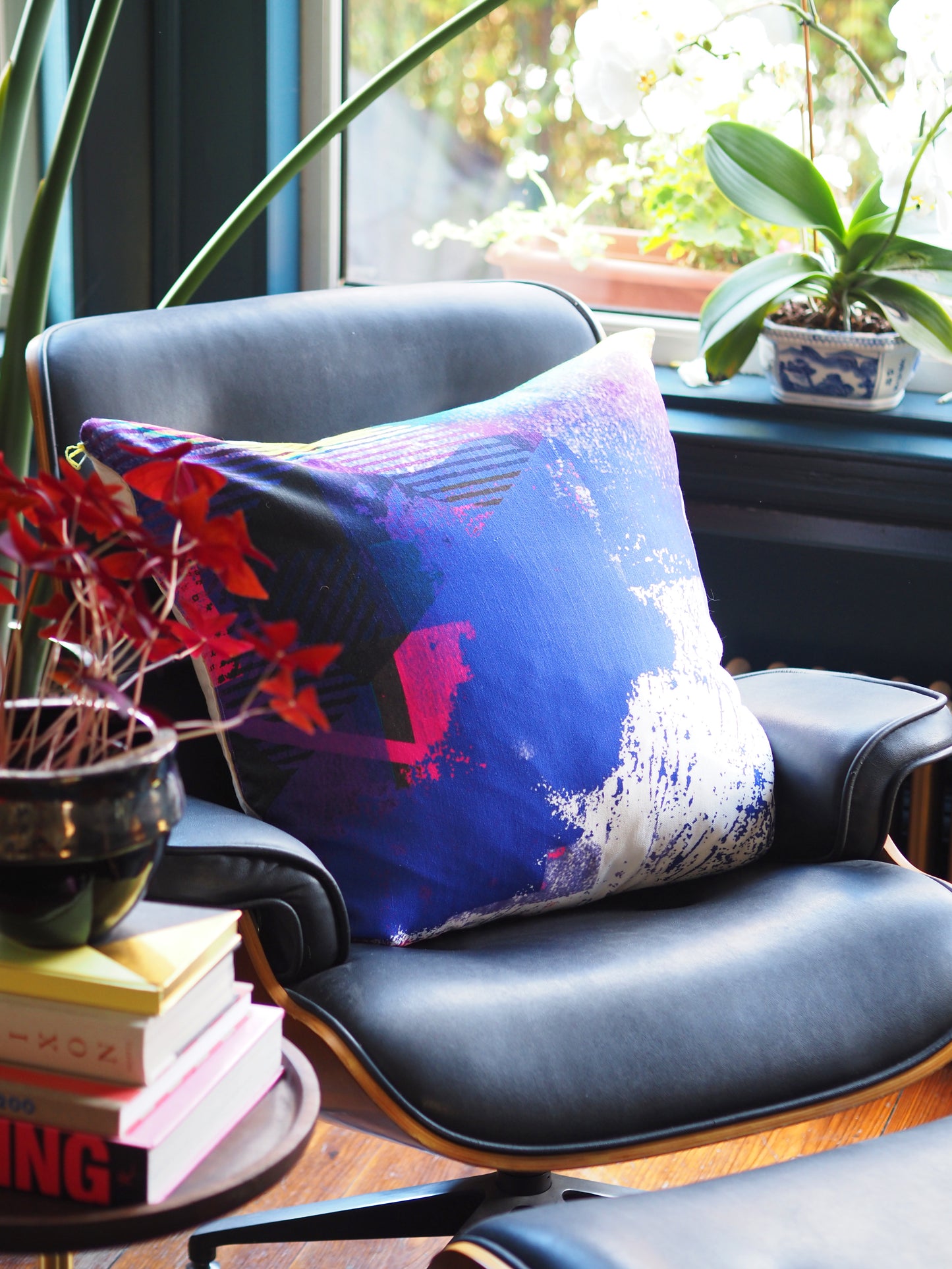 Decorative pillow on a chair with a window and plants in the background