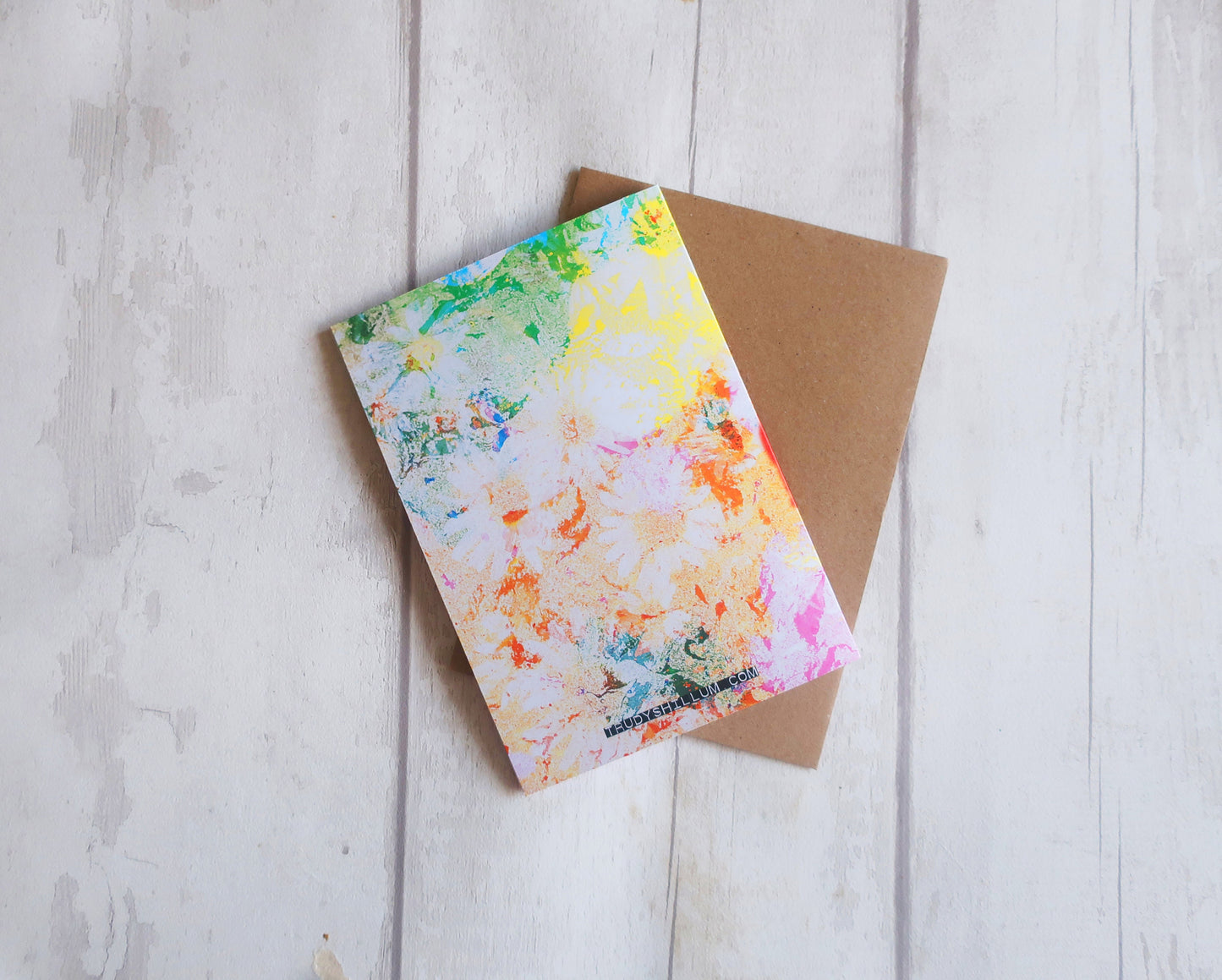 Colorful watercolor card and brown envelope on a light wooden surface
