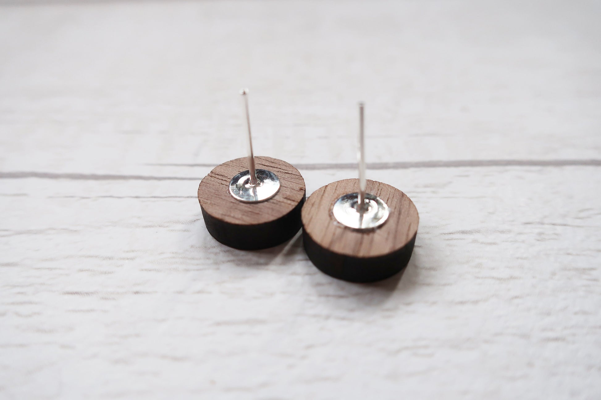 Two wooden earrings with metal components on a light wooden surface