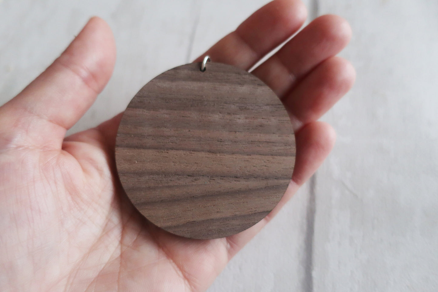 Wooden round pendant held in a hand against a light background