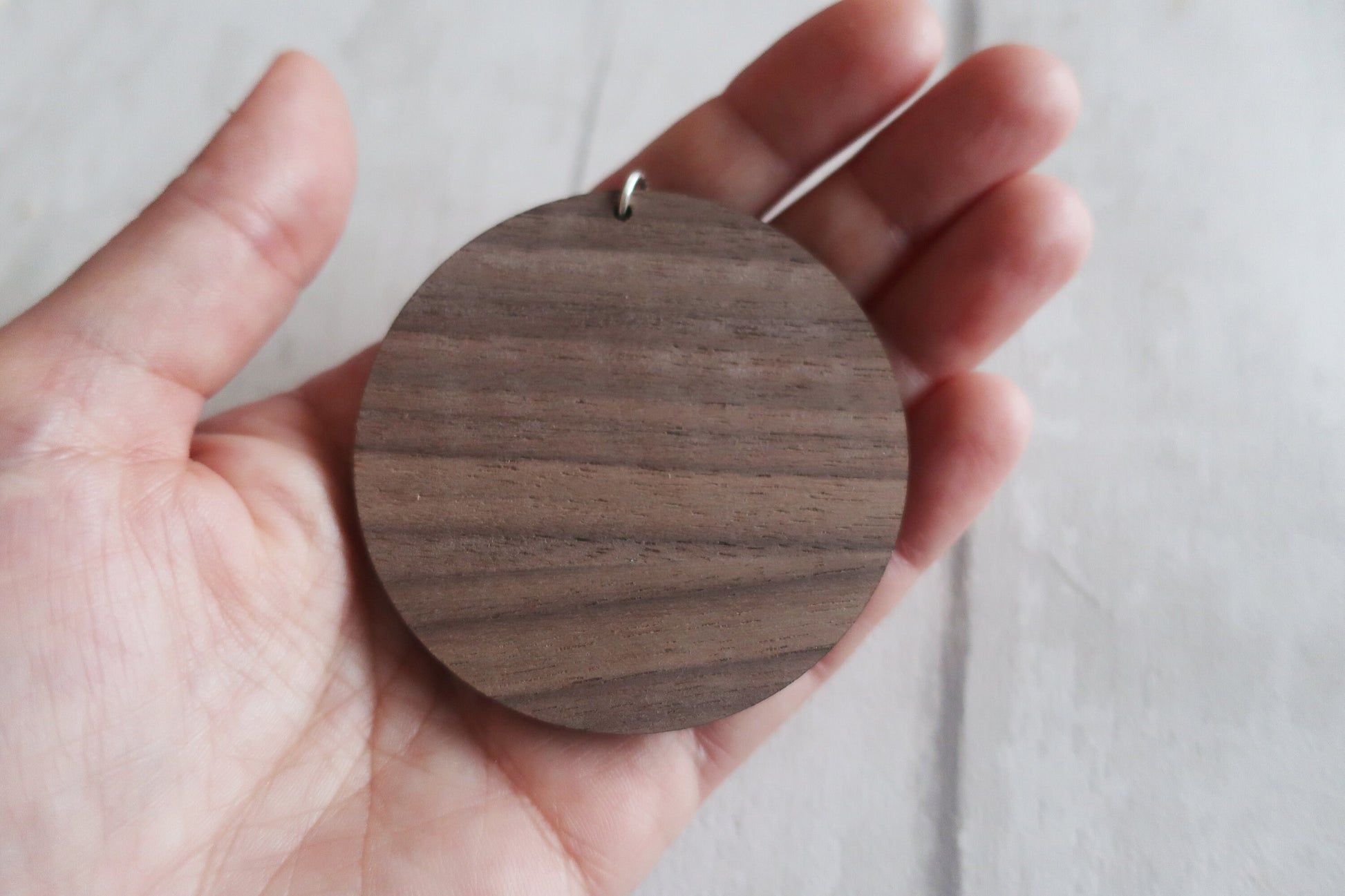 Wooden round pendant held in a hand against a light background