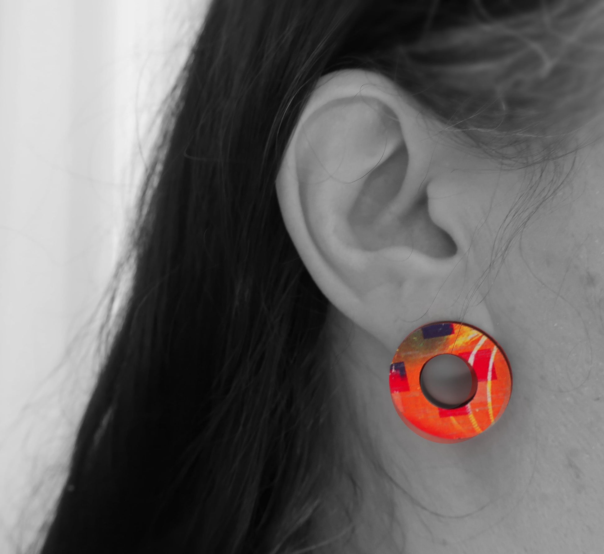 Close-up of an ear wearing a colorful round earring with a blurred background
