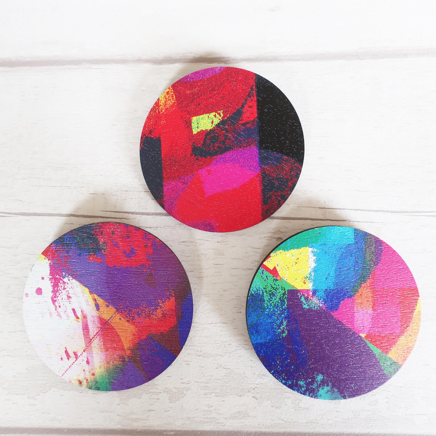 Three colorful circular brooches on a white wooden surface