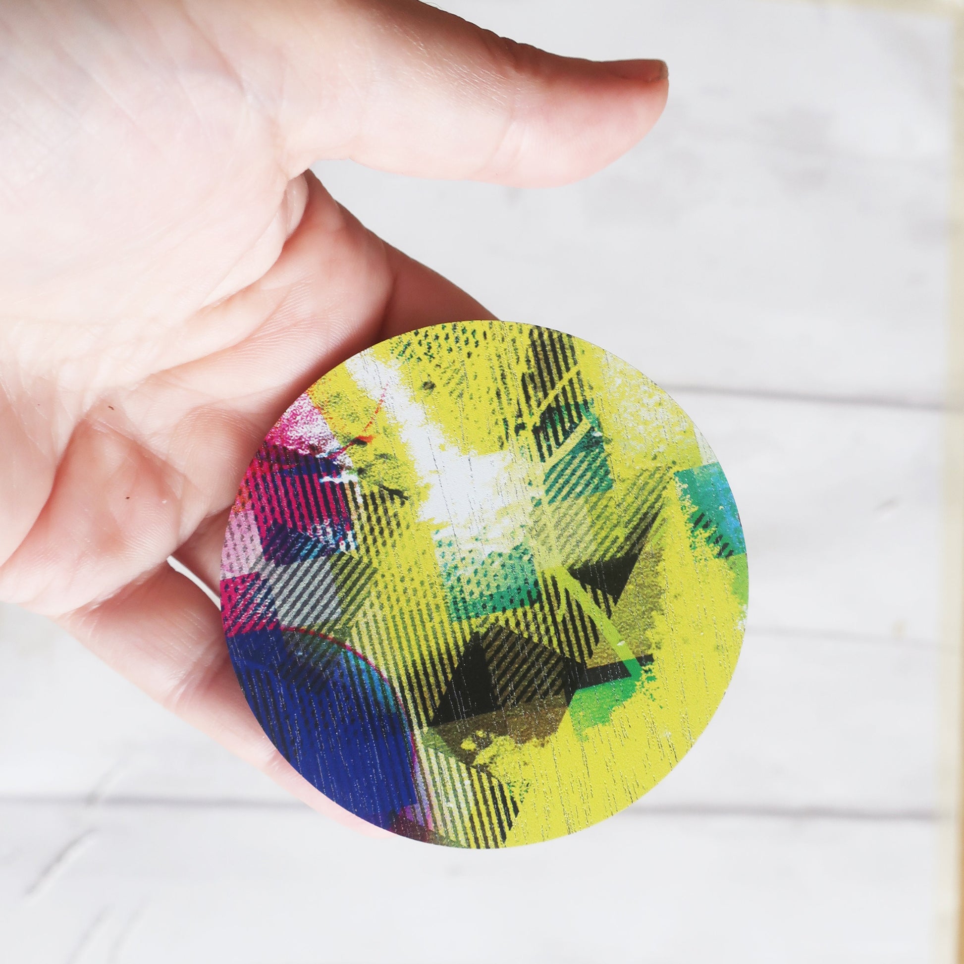 Colorful circular brooch held by a hand on a white background
