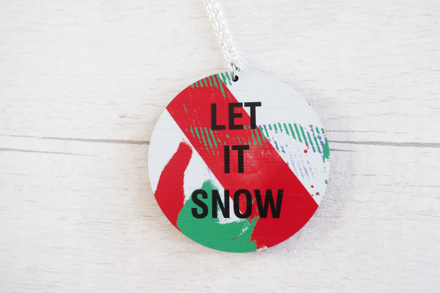 Round decorative necklace  with 'LET IT SNOW' text on a white wooden background