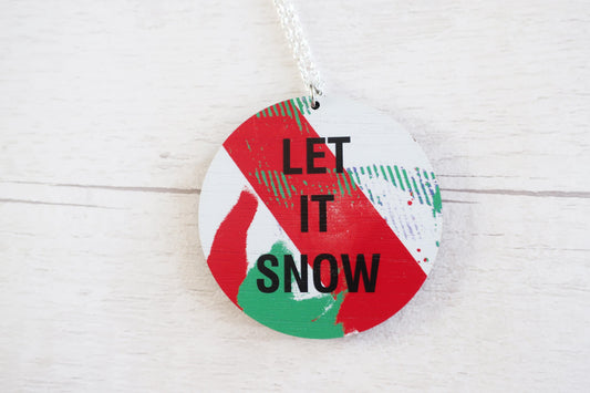Round decorative necklace  with 'LET IT SNOW' text on a white wooden background