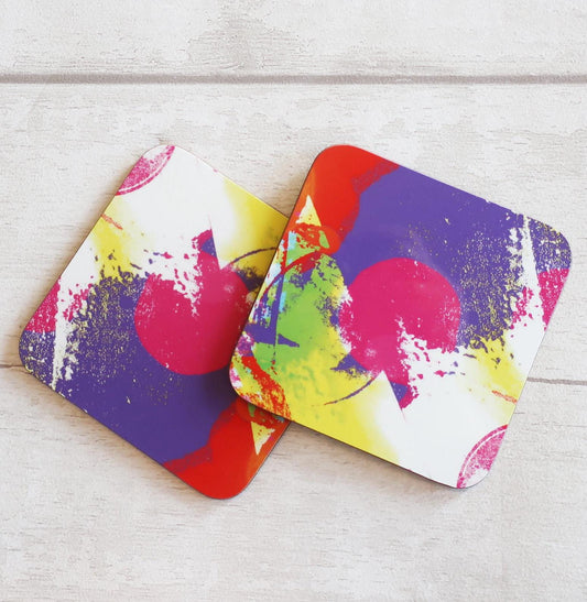 Two colorful coasters with abstract designs on a light wooden surface