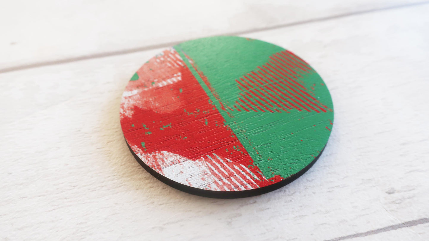 Round brooch with red and green abstract design on a white wooden surface