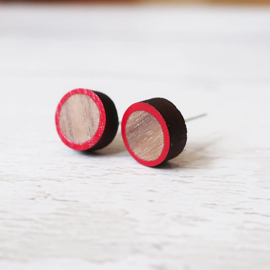 Round wooden earrings with red and black borders on a white surface