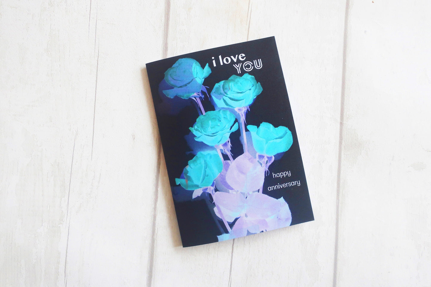 Greeting card with blue roses and 'I love you' text on a white wooden surface