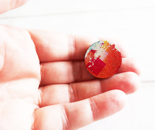 Hand holding a small round pin badge with a colorful pattern on a white background