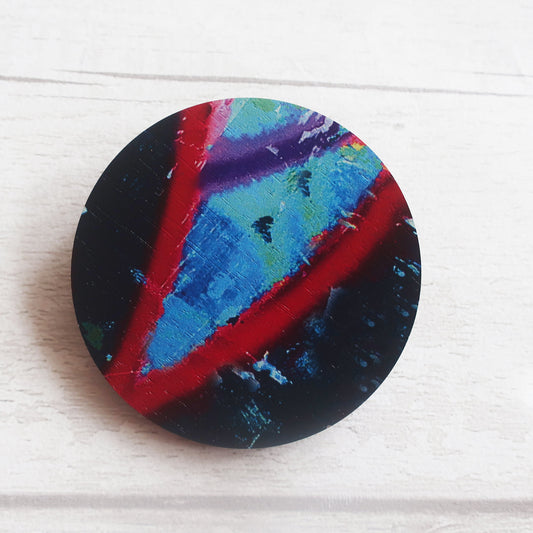 Colorful circular brooch with a black background on a white wooden surface