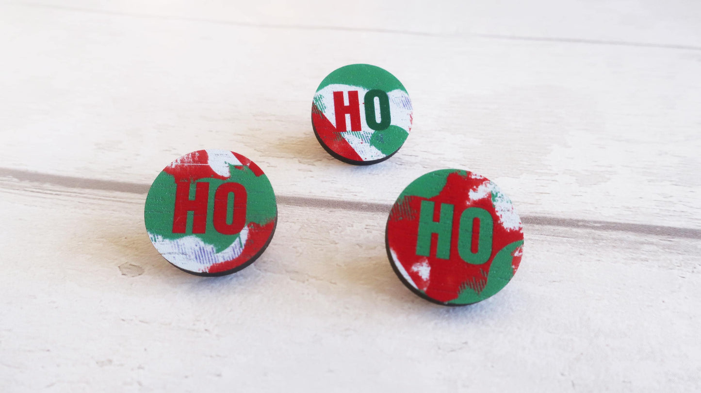 Three round pin badges with 'HO' text on a wooden surface