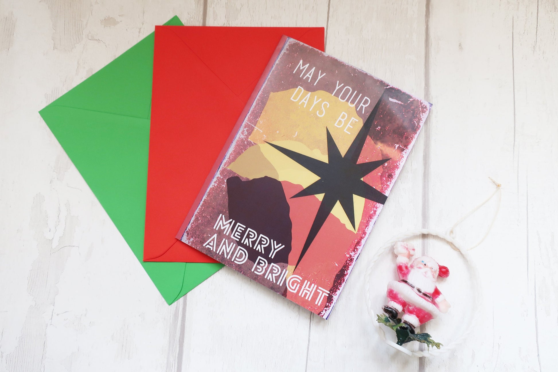 Christmas card with 'May your days be Merry and Bright' text, surrounded by red and green envelopes on a wooden surface.