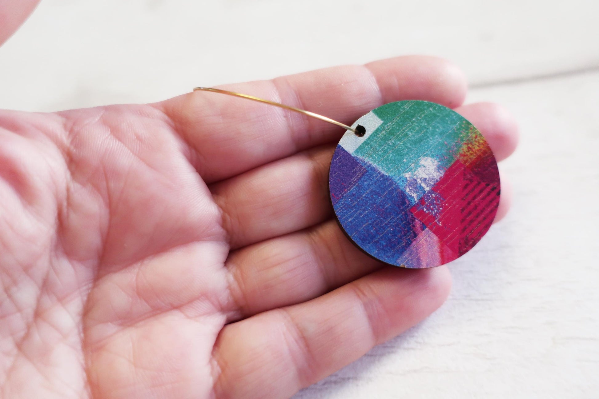 Colorful circular earring held in a hand against a white background
