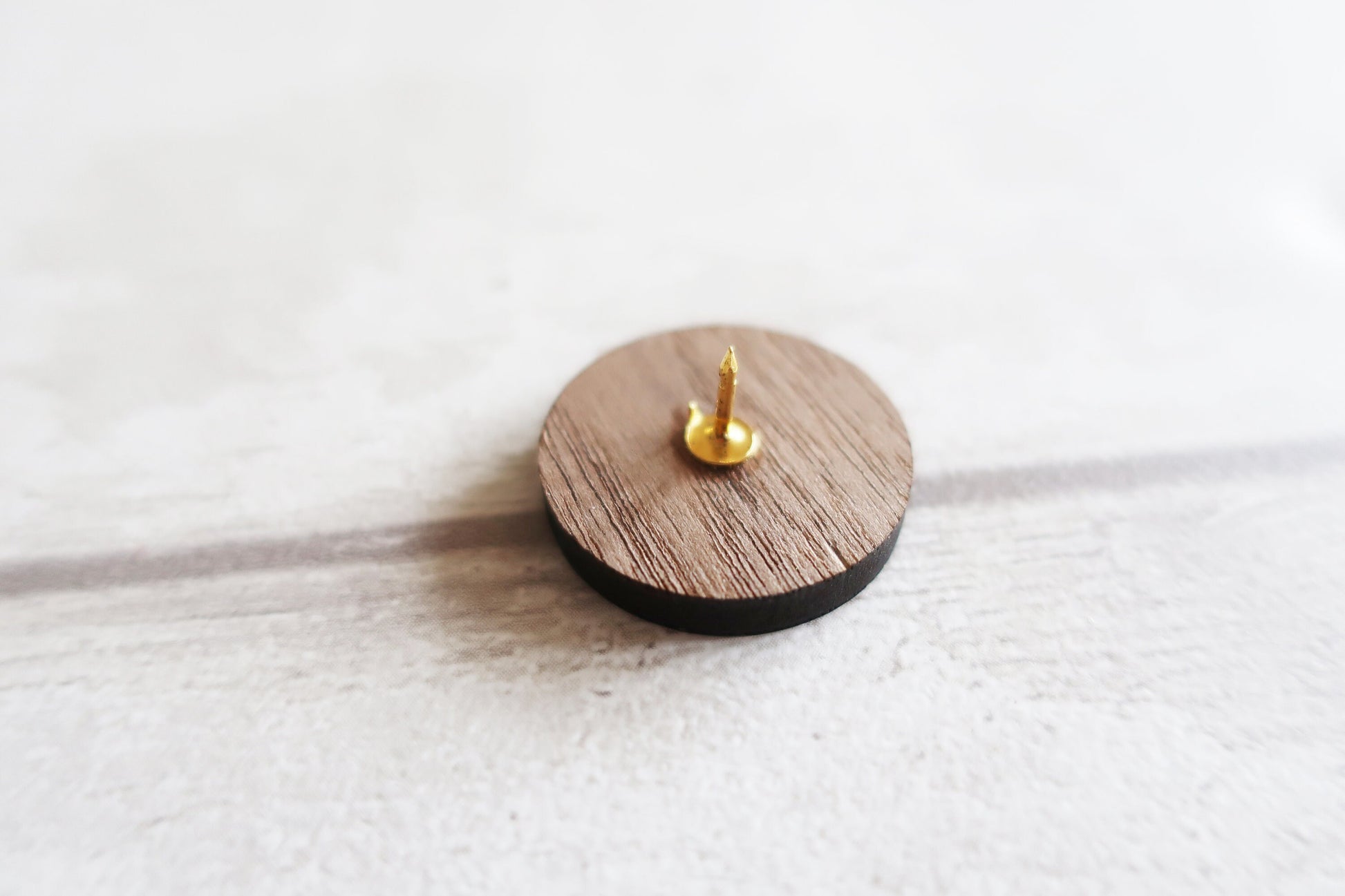 Wooden and black cylindrical pin badge back with a gold spike on a white background