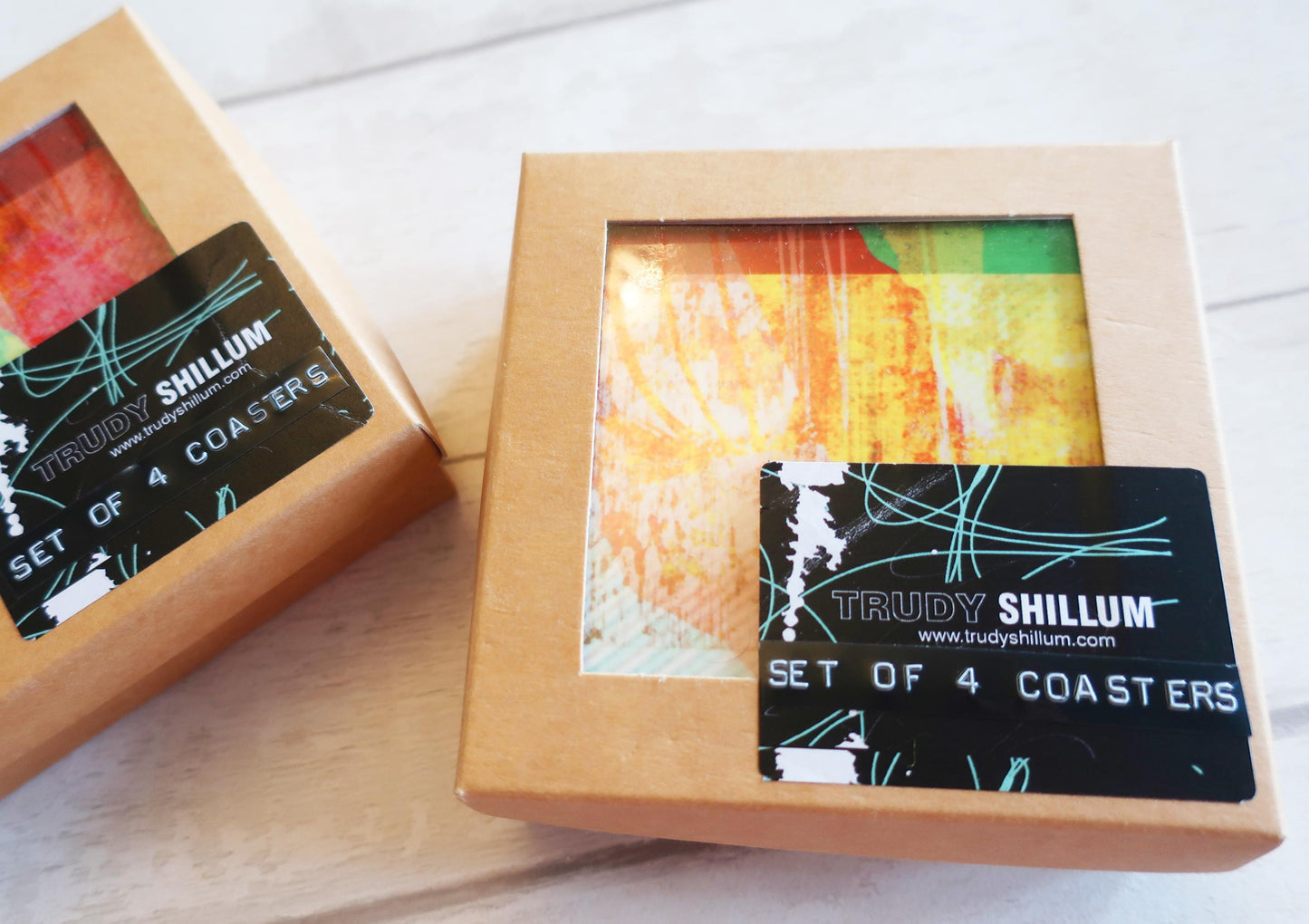 Two boxes of Trudy Shillum coasters on a wooden surface
