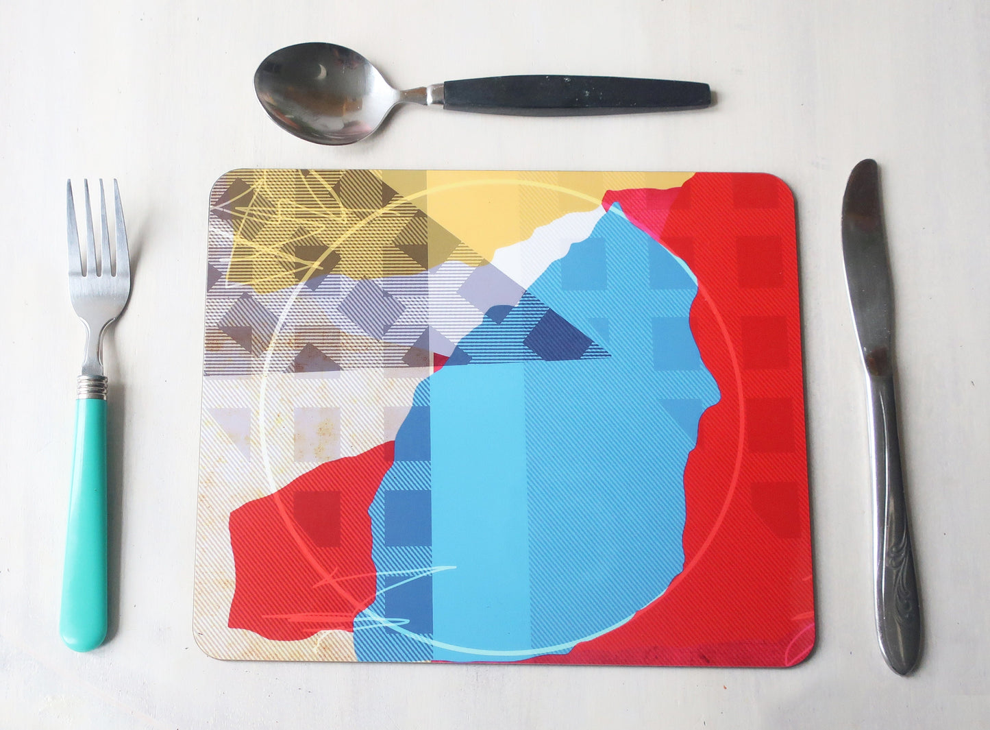 Colorful placemat with abstract design on a white surface with cutlery.